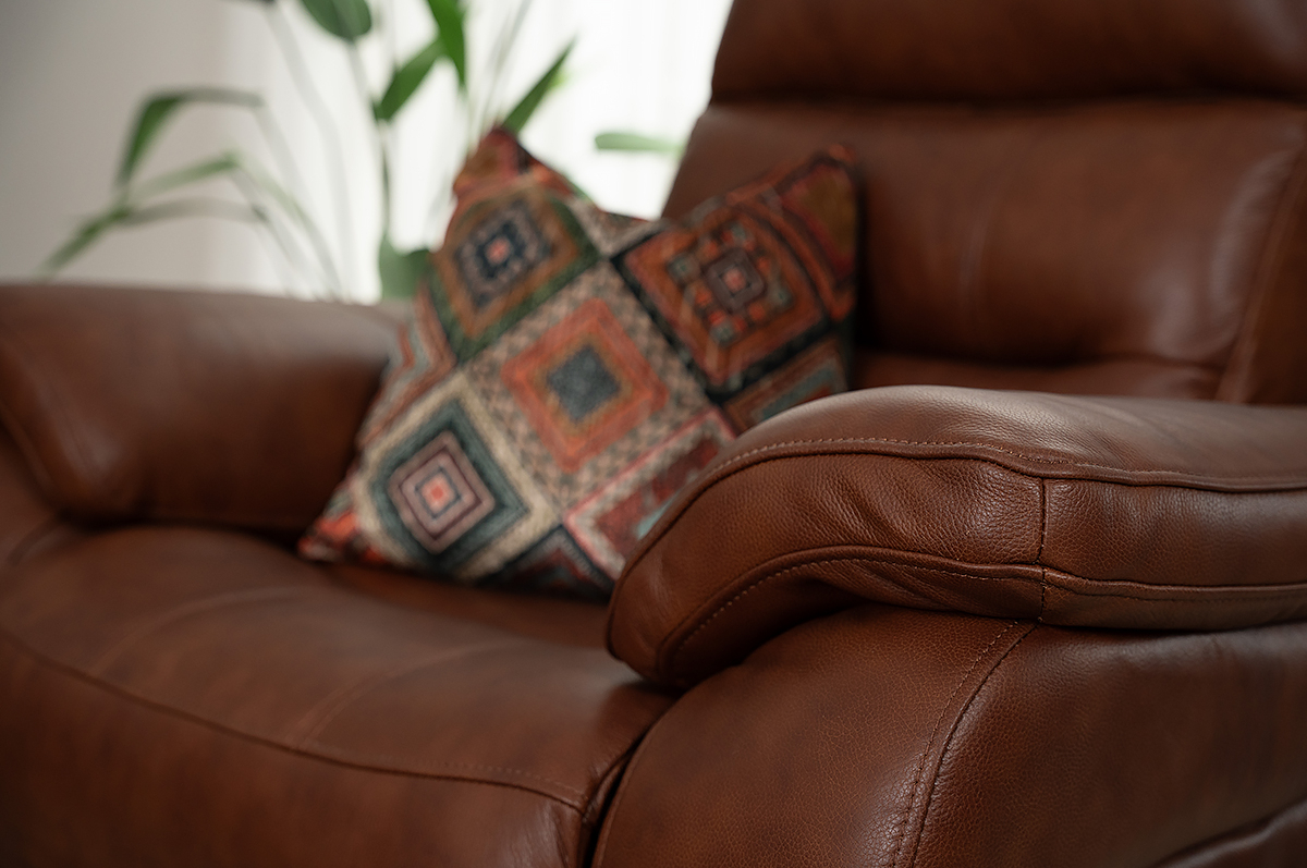 close-up of brown leather sofa with a colourful cushion resting on the leather sofa arm